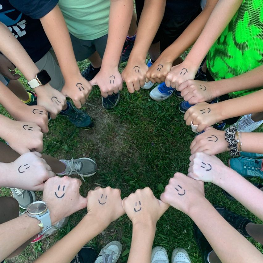 Eine Gruppe von Kindern und Jugendlichen bildet einen Kreis auf einem Rasenfeld mit smiley Gesichtern auf den Händen gezeichnet.