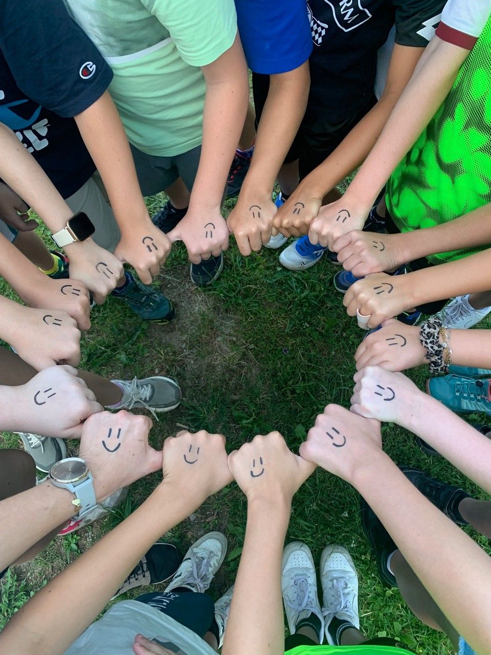 Eine Gruppe von Kindern und Jugendlichen bildet einen Kreis auf einem Rasenfeld mit smiley Gesichtern auf den Händen gezeichnet.