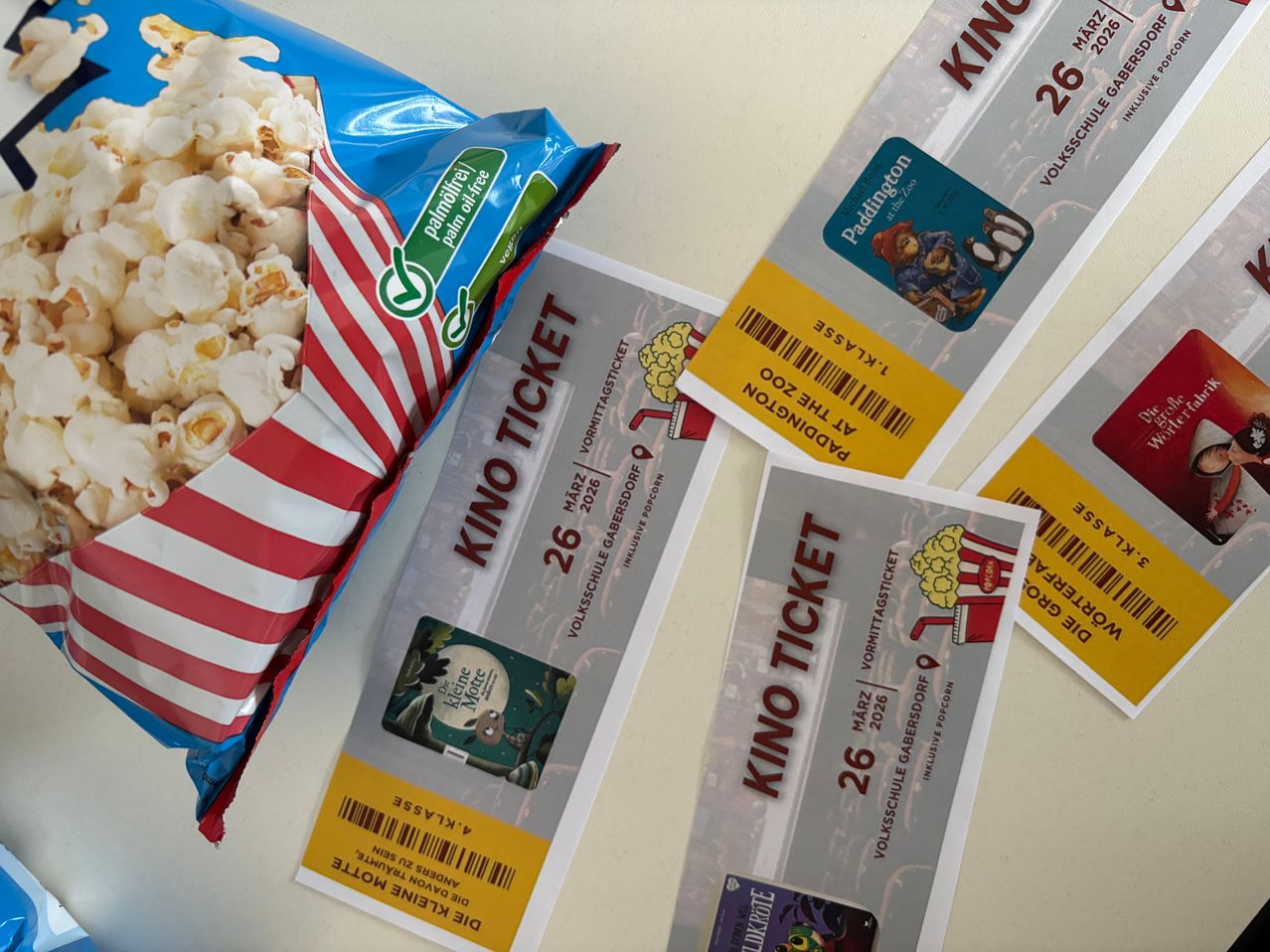 Eine Tüte Popcorn, gekennzeichnet als 'Palmölfrei', liegt neben drei Kinotickets, eines mit einem Paddington-Bild und die anderen mit einem Charakter im mondbeschienenen Wald.
