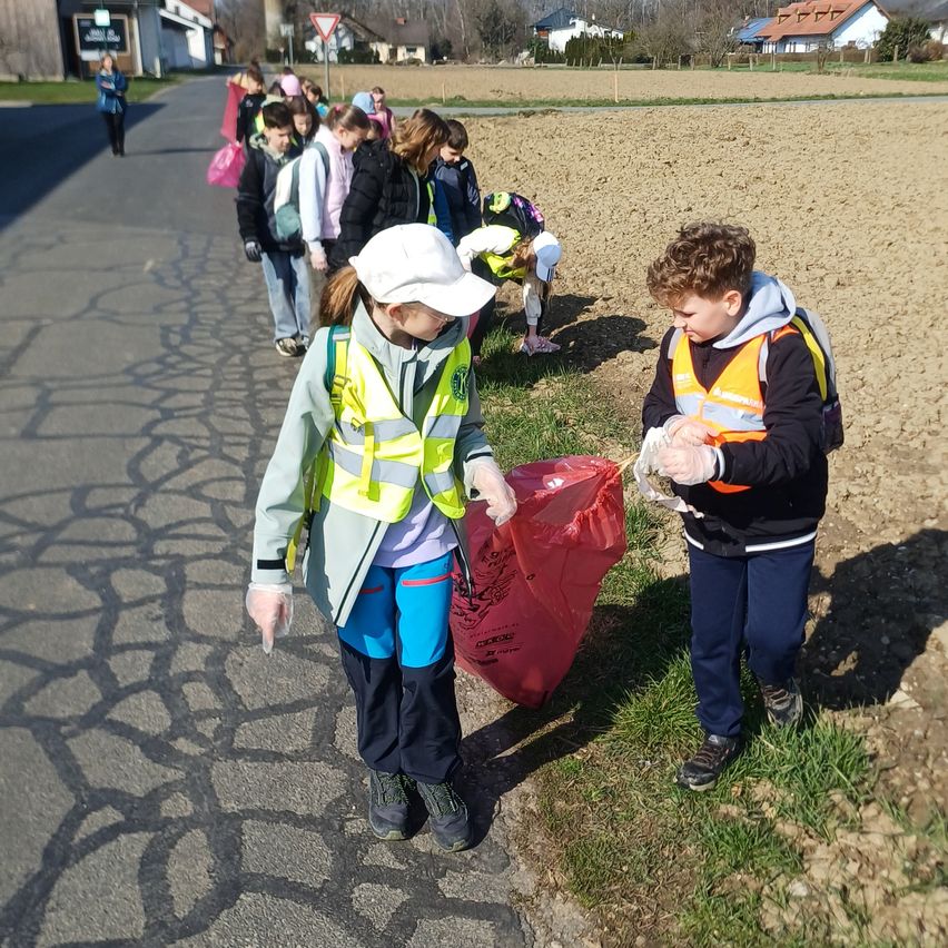 Eine Gruppe von Kindern läuft am Straßenrand, trägt Sicherheitswesten und Handschuhe und trägt rote Taschen. Sie nehmen an einer Aufräumaktion teil.