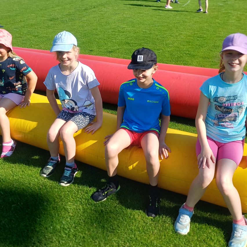 Vier Kinder sitzen auf einem gelben aufblasbaren Hindernis. Drei sind Mädchen und eines ist ein Junge. Sie alle lächeln und scheinen für ein Foto zu posieren.