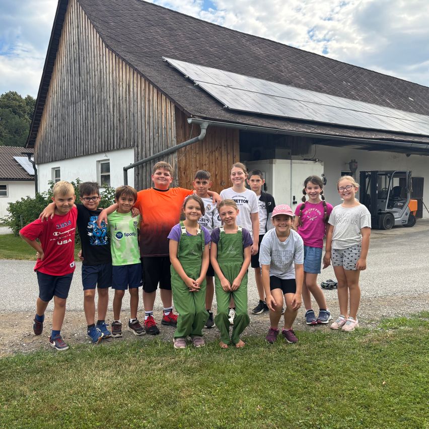 Eine Gruppe von Kindern posiert vor einem Scheunen mit Solarpanelen auf dem Dach unter einem bewölkten Himmel.
