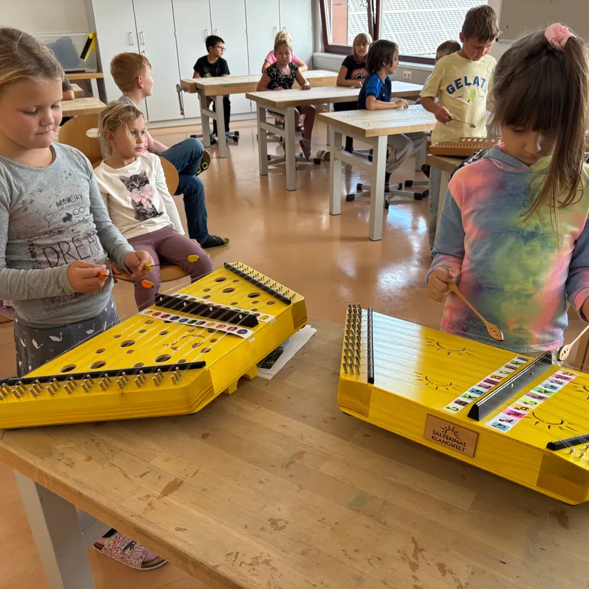 Mehrere Kinder spielen ein großes gelbes Musikinstrument in einer Klassenzimmerumgebung.
