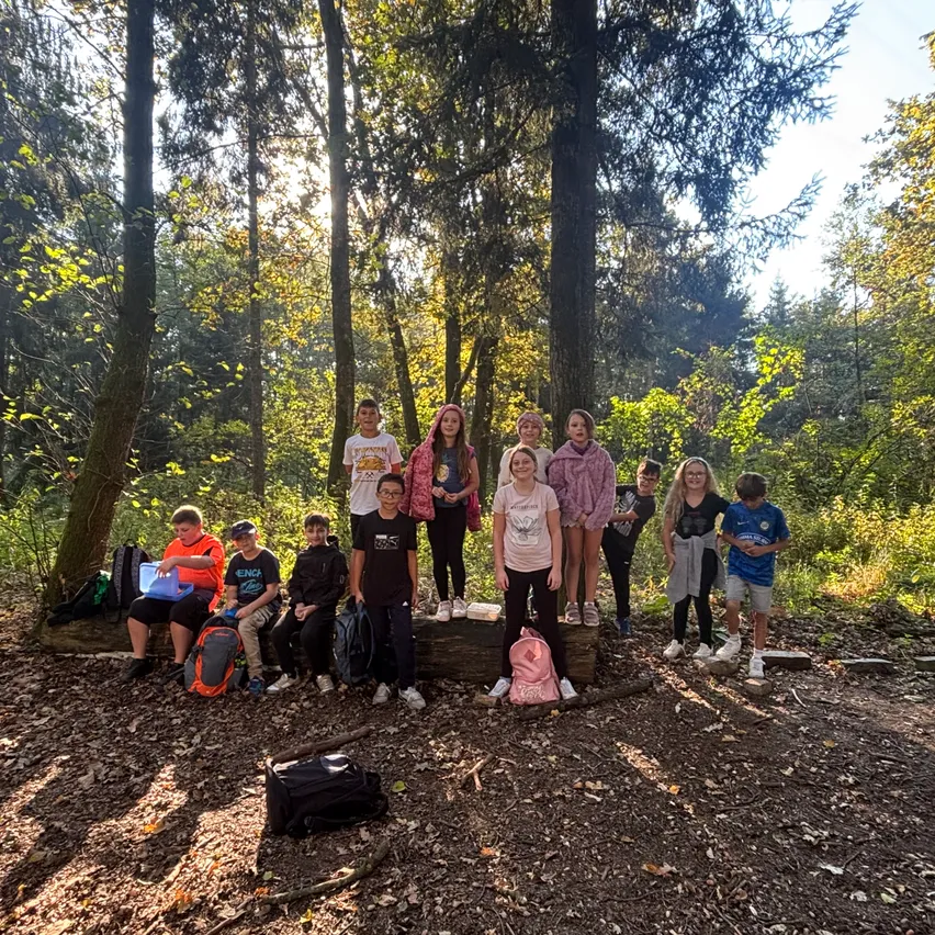 Eine Gruppe von Kindern und Jugendlichen steht und sitzt in einem Wald und posiert für ein Foto.