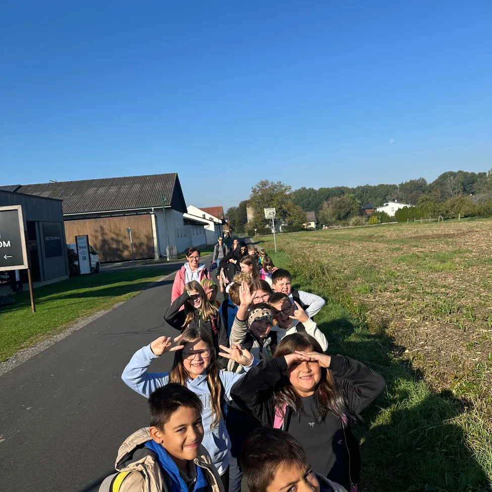 Eine Gruppe von Kindern, einige mit Brille, gehen in einer Reihe auf einer Straße, wobei ein Kind ein Friedenszeichen macht.
