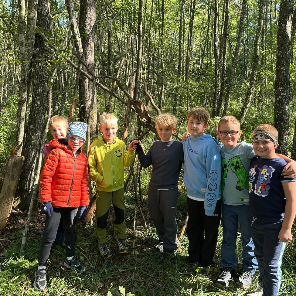 Eine Gruppe von Kindern, die verschiedene Jacken und Hosen tragen, steht zusammen im Wald.