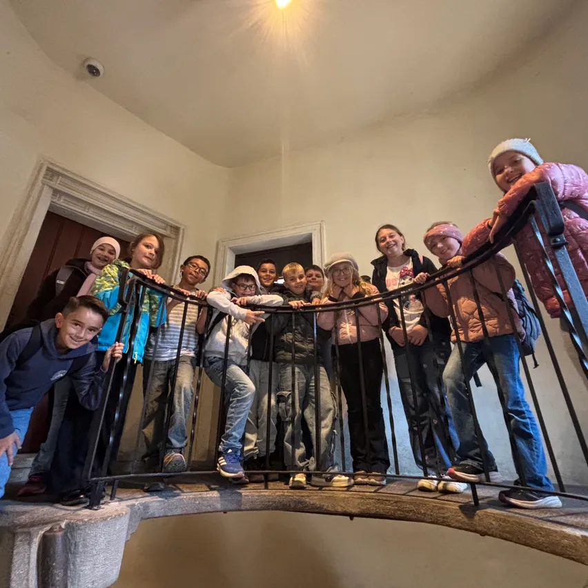 Eine Gruppe von Kindern und Jugendlichen steht auf einer Wendeltreppe, lächelt und posiert für ein Foto.