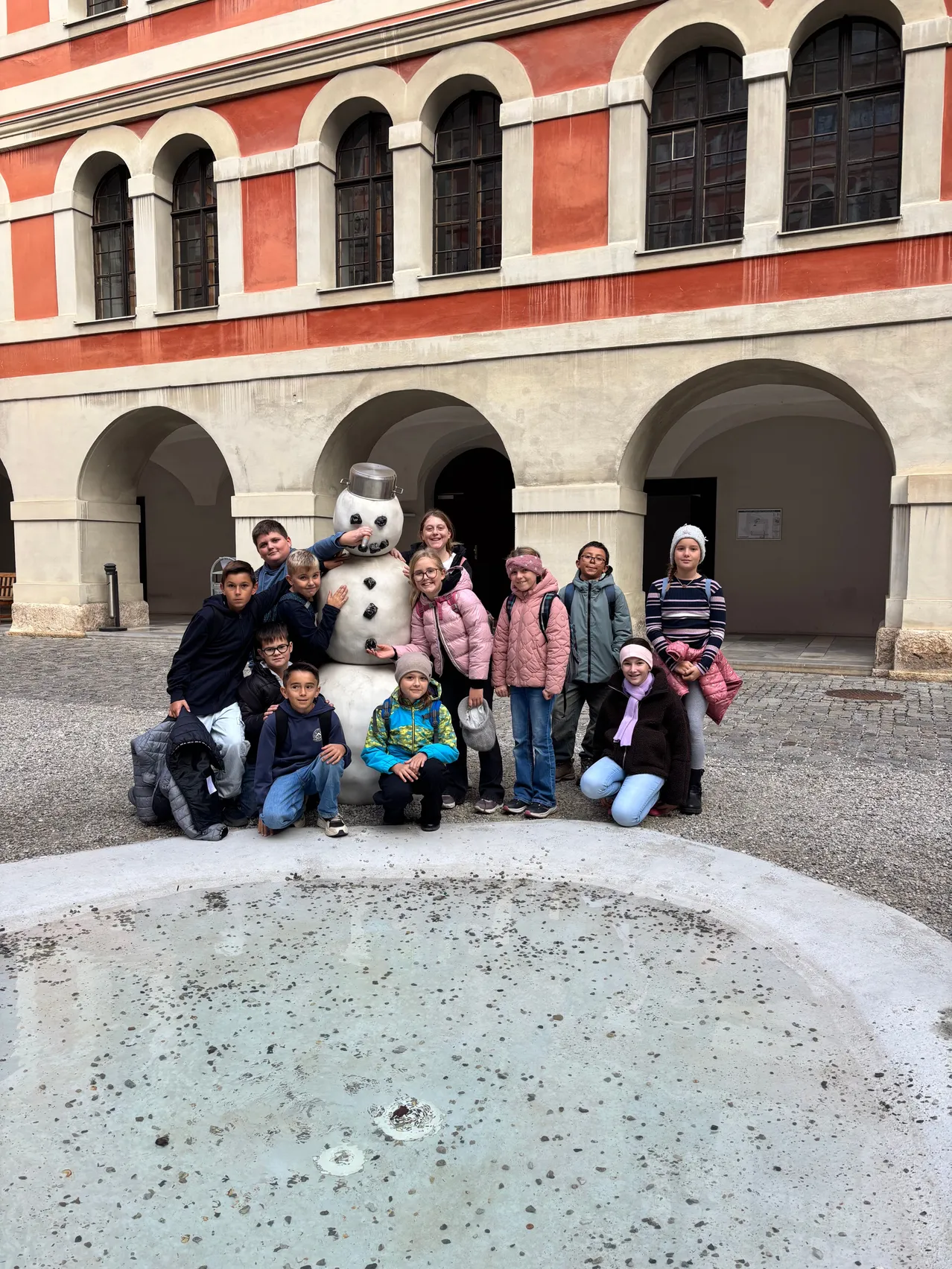 Eine Gruppe von Kindern und Erwachsenen posiert für ein Foto vor einem Schneemann vor einem Gebäude.