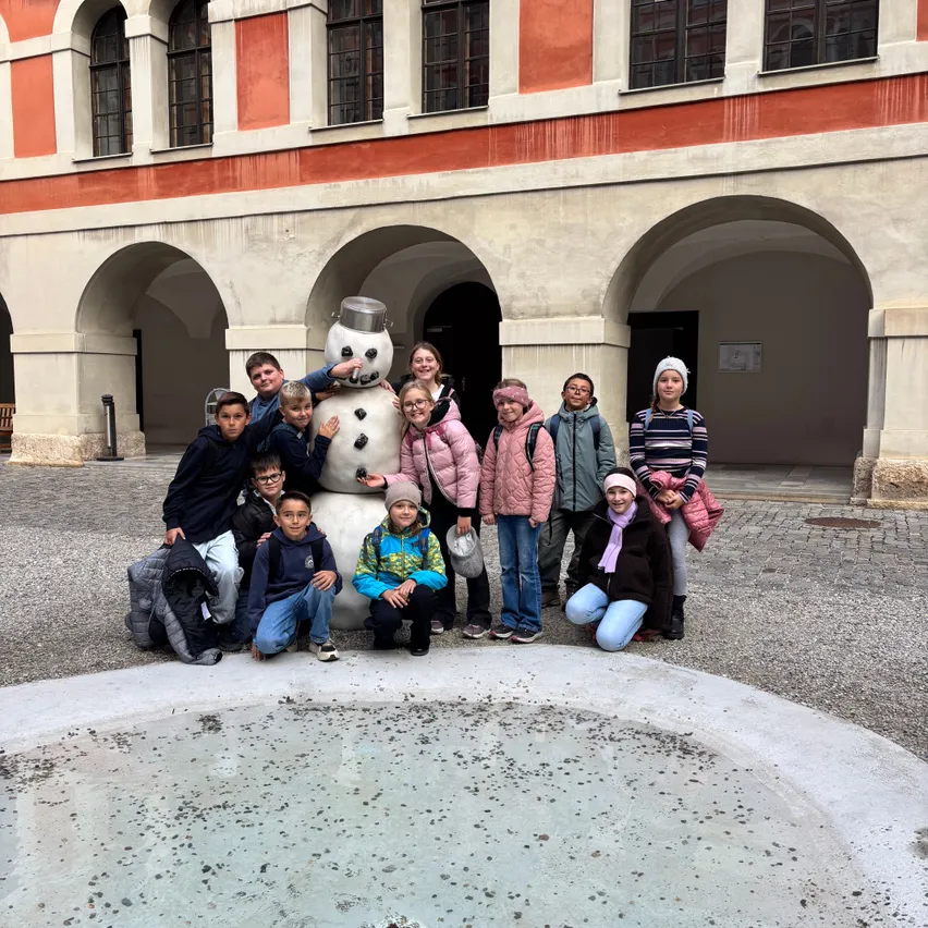 Eine Gruppe von Kindern und Erwachsenen posiert für ein Foto vor einem Schneemann vor einem Gebäude.