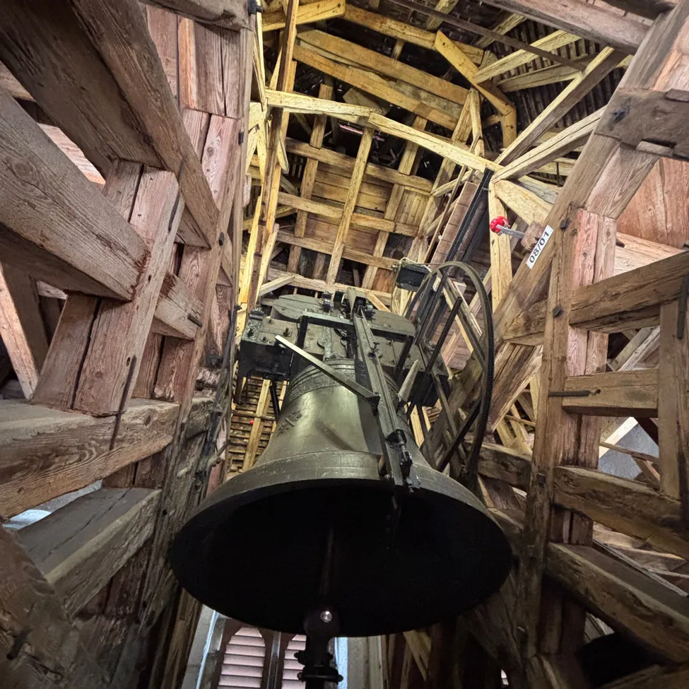 Eine große Glocke ist von der Decke einer Holzstruktur aufgehängt.
