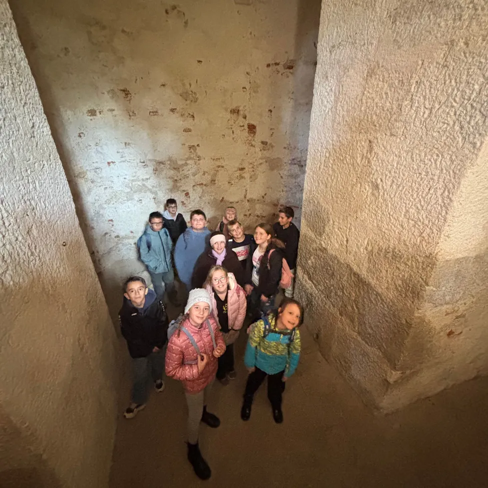 Eine Gruppe von Kindern und Erwachsenen steht in einem engen, schwach beleuchteten Tunnel mit Steinmauern.
