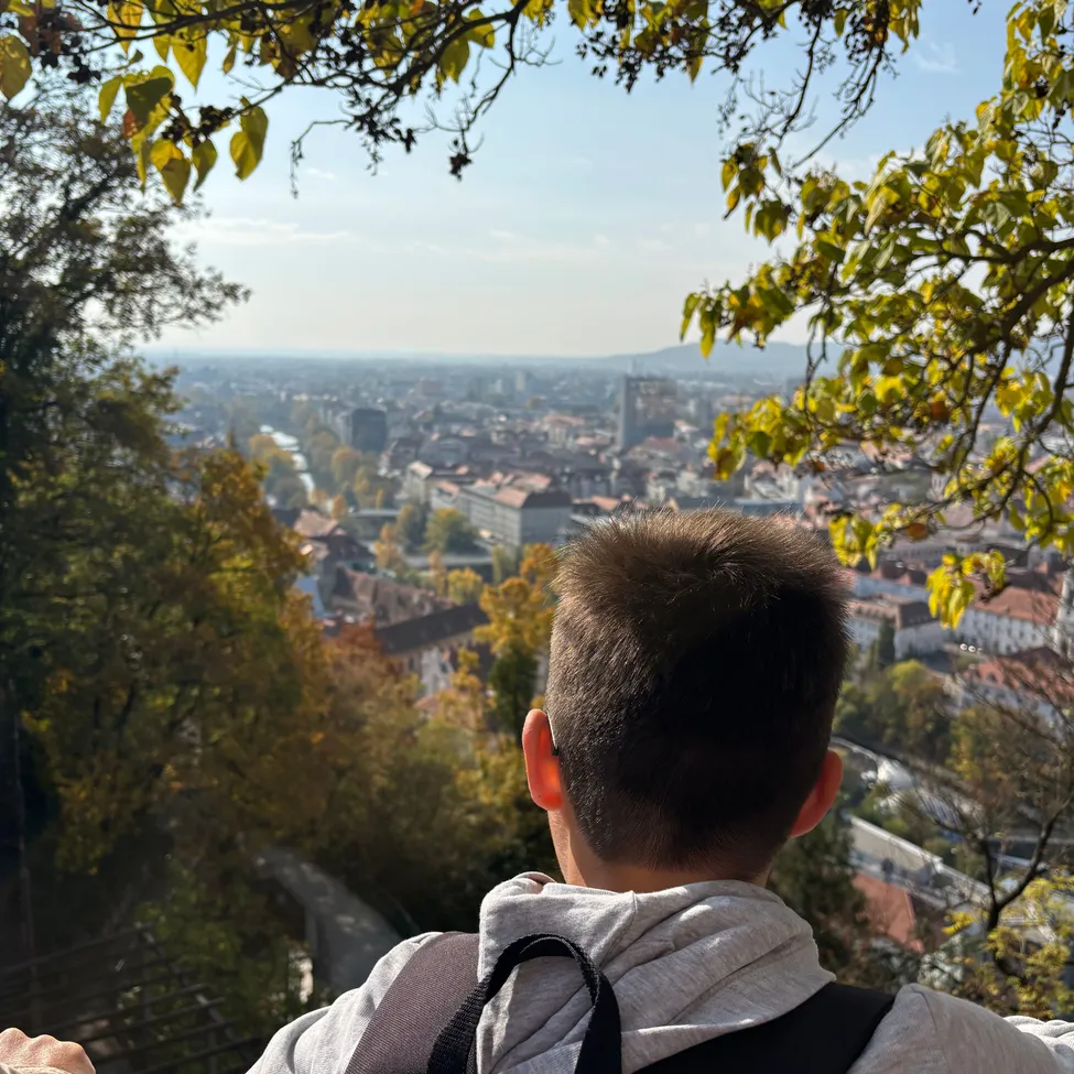 Ein Junge mit Rucksack schaut von einem hohen Aussichtspunkt auf eine Stadt.