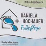Das Logo für einen mobilen Fußpflegedienst zeigt ein Haus mit einem Fußabdruck, einem Vogel und dem Text Daniela Hochauer Fußpflege. Das Logo hat eine blau-weiße Farbgebung.