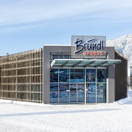 Die Vorderseite eines Sportgeschäfts mit einem Holzzaun, einer Glastür und einem Schild, das Brundl Sports steht.