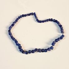 Eine Halskette aus blauen Perlen wird auf einer weißen Oberfläche in Herzform angeordnet präsentiert. Die Perlen variieren in Größe und Form.