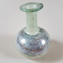 Eine antike Glasvase mit grünlich-blauer Farbe, einem schmalen Hals und einem kugelförmigen Körper, die auf einer weißen Oberfläche ruht.