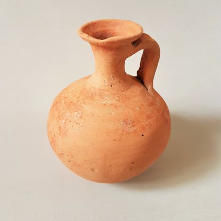 Eine alte Terrakotta-Krug mit einem Henkel auf weißem Hintergrund, der Anzeichen von Alter mit weißen Flecken aufweist.