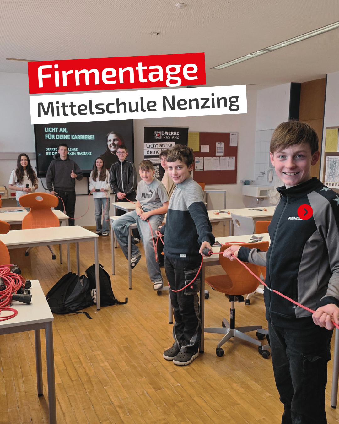 Schüler der Mittelschule Nenzing nehmen an einer praktischen Aktivität teil. Sie halten ein rotes Kabel, während andere an den Tischen zusehen. Ein Banner trägt die Aufschrift Firmentage Mittelschule Nenzing.