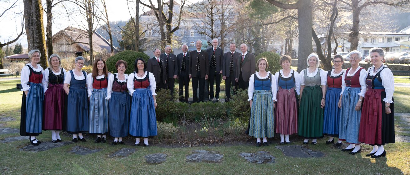 Eine Gruppe von Menschen in traditioneller Kleidung steht in einem Garten, umgeben von Bäumen und Büschen. Sie posieren für ein Foto.