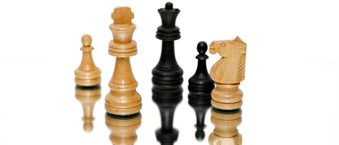 Eine Reihe von Schachfiguren mit hellbraunen und schwarzen Stücken, reflektiert auf einer weißen Oberfläche.