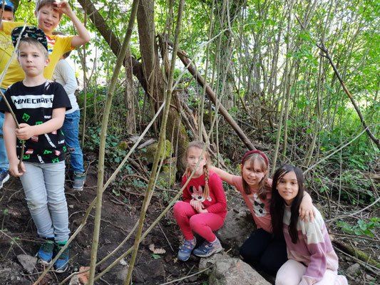 Eine Gruppe von Kindern steht und hockt in einem Wald, wobei drei Mädchen vorne lächelnd für die Kamera posieren.