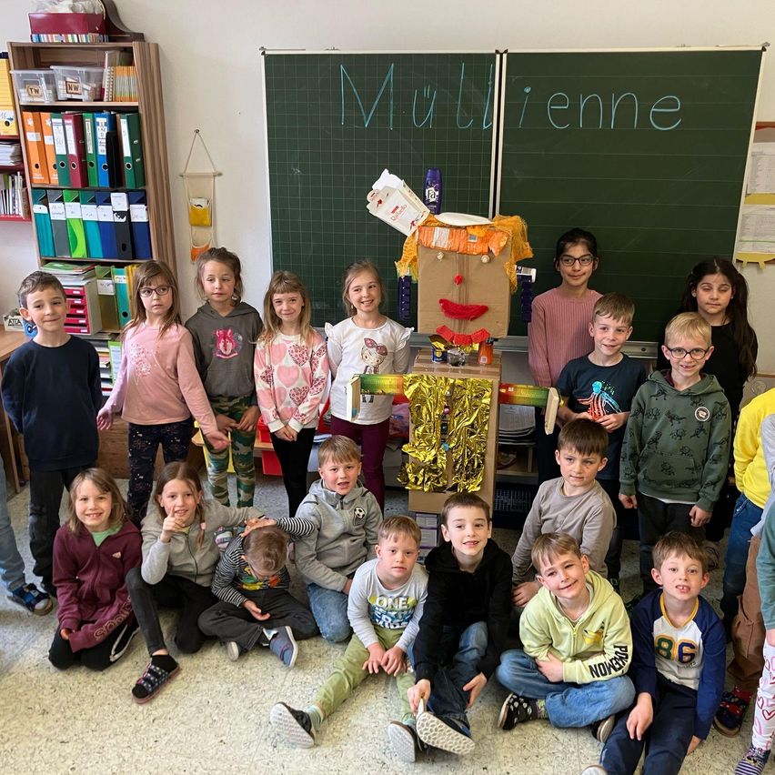 Gruppe von Kindern, die für ein Foto in einem Klassenzimmer posieren, mit einer Tafel, auf der 'Multii ene' auf Französisch steht.
