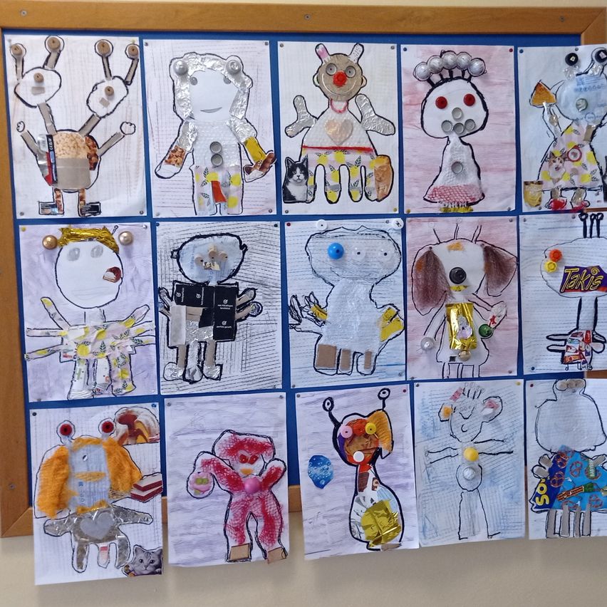 Ein Bulletin-Board zeigt eine Sammlung bunter Zeichnungen verschiedener Charaktere, darunter Roboter, Tiere und Menschen, die jeweils mit Knöpfen, Papier und anderen Materialien verziert sind.