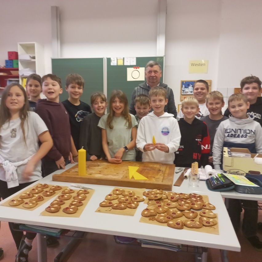 Eine Gruppe von Kindern und ein Mann stehen um einen Tisch mit Keksen darauf. Der Mann lächelt und die Kinder posieren für ein Foto.