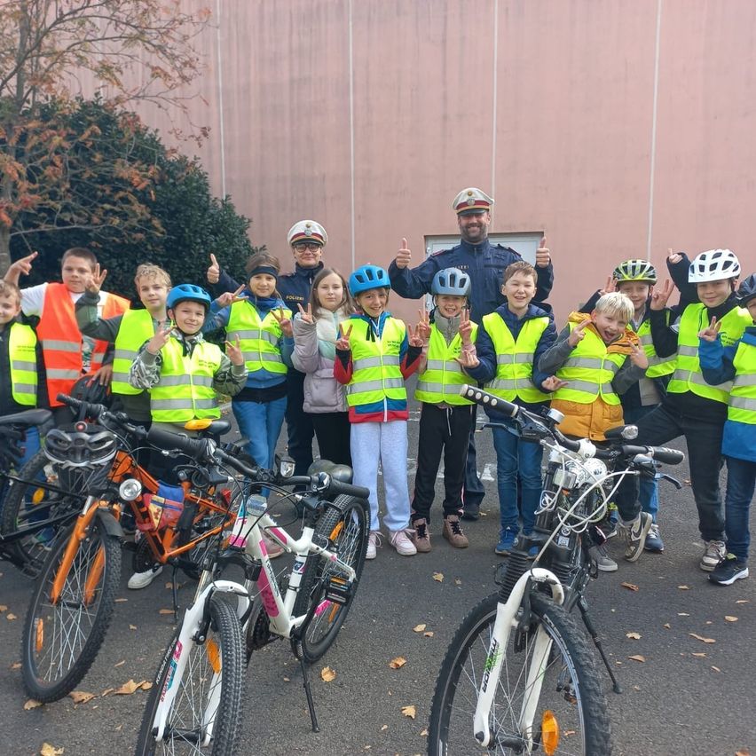Gruppe von Kindern mit Sicherheitswesten und Helmen, die mit Polizeibeamten vor Fahrrädern posieren.