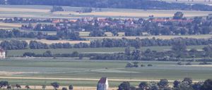 Luftaufnahme einer ländlichen Landschaft mit Feldern, Bäumen und einem kleinen Dorf. Ein einzelnes Haus steht in der Mitte der Felder.