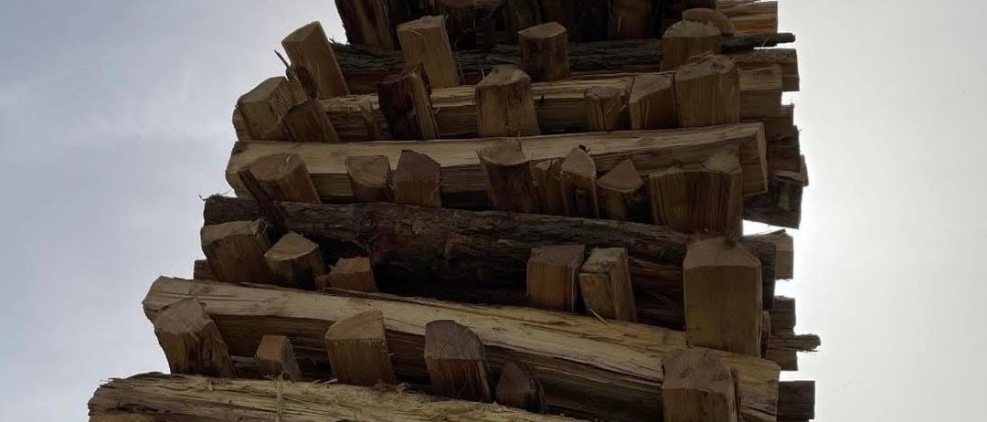 Ein Stapel Holzscheite ist für ein Lagerfeuer arrangiert, mit einem Kreuz obenauf. Das Datum 04. April 2026 steht links. Der Text lautet: 'Für ein reichhaltiges Feuer und Toast ist gesorgt! Eure FF Deutsch Schützen.' Der Himmel ist bewölkt.