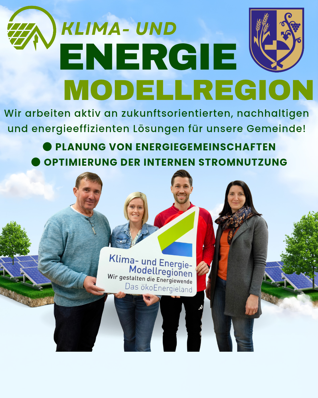 Vier Personen stehen mit einem Schild, auf dem 'Klima-und Energie-Modellregionen' steht, unter blauem Himmel. Solarpanele sind im Hintergrund zu sehen.