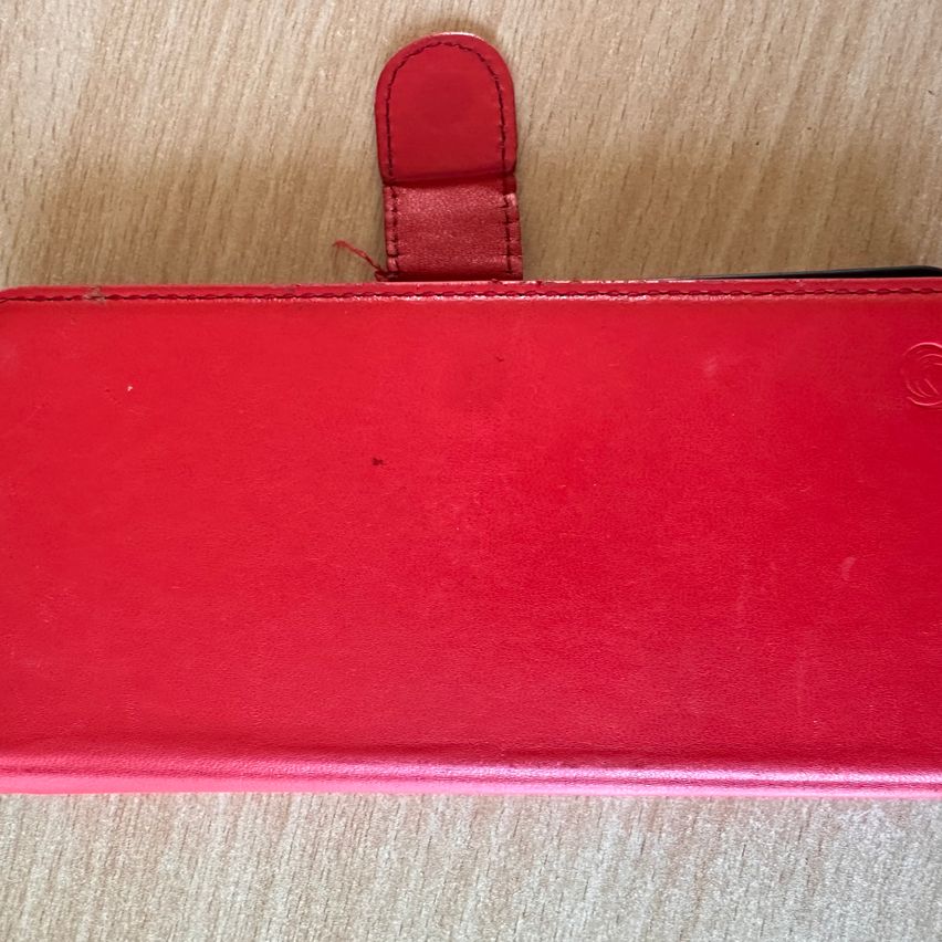 Rotes Lederetui mit Lasche und Logo auf Holzhintergrund