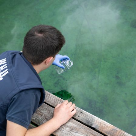 Ein Mann in blauer Uniform und Handschuhen entnimmt Wasser aus einem See.