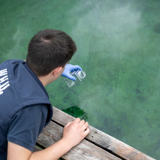 Ein Mann in blauer Uniform und Handschuhen entnimmt Wasser aus einem See.