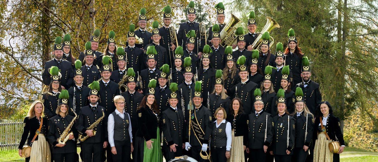 Eine Gruppe von Musikern in einheitlichen Kostümen posiert für ein Foto. Sie halten verschiedene Instrumente wie Trompete, Saxophon und Trommel.