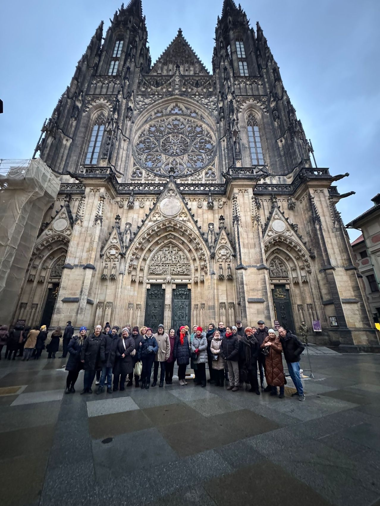 Eine Gruppe von Menschen in Winterkleidung posiert für ein Foto vor einer großen gotischen Kathedrale mit kunstvollen architektonischen Details.
