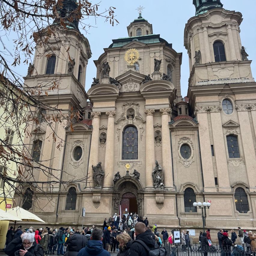 Eine große Kirche mit zwei Türmen und vielen Statuen ist zu sehen. Viele Menschen haben sich vor der Kirche versammelt.