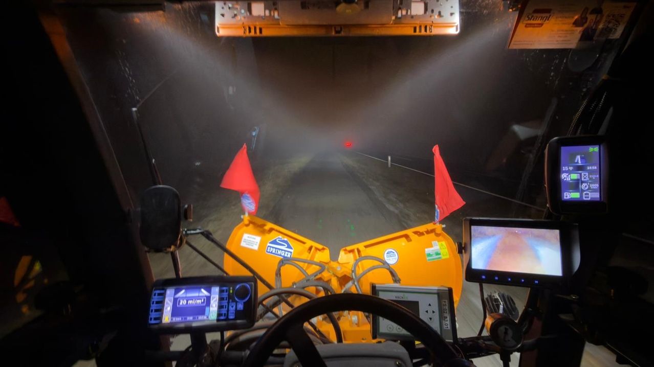 Blick aus dem Inneren eines Fahrzeugs, das durch einen Tunnel fährt, mit einer gelben Maschine, roten Flaggen, einem Bildschirm und einem Lenkrad.