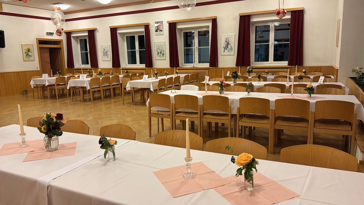 Ein Esszimmer mit mehreren Tischen, die jeweils mit Blumen, Kerzen und Stoffservietten bestückt sind. Der Raum verfügt über Holzstühle, weiße Wände und Bilderrahmen. Der Boden ist aus Holz.