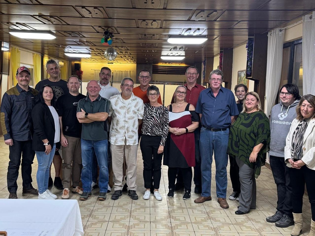A group of people, both men and women, are standing together in a room. They are all smiling and posing for a photo.