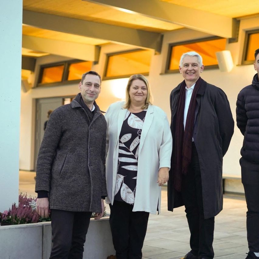 Four individuals pose together outside a modern building with arched windows, smiling for a photo.