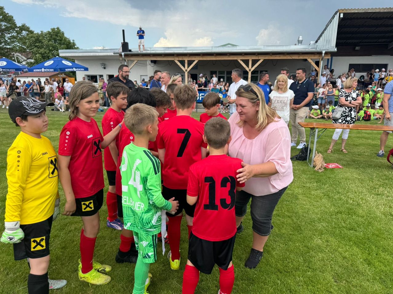 Gruppe junger Fußballer in roten und grünen Trikots unterhält sich vor einer jubelnden Menge bei einer Outdoor-Veranstaltung.