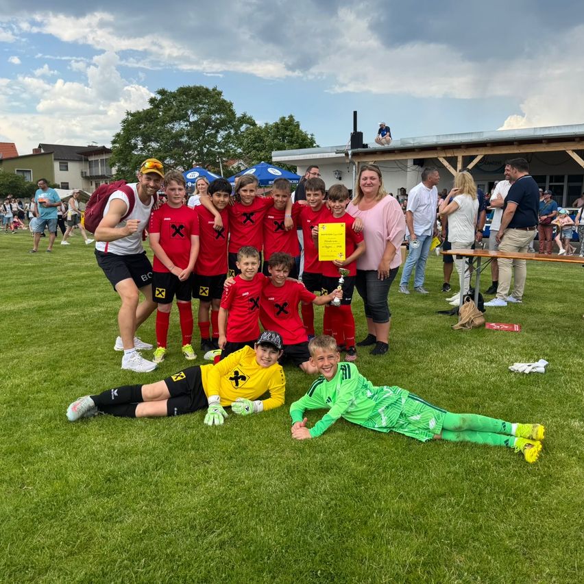 Eine Fußballmannschaft mit Kindern, Erwachsenen und einer Frau mit einem Pokal posiert auf einem grünen Feld.