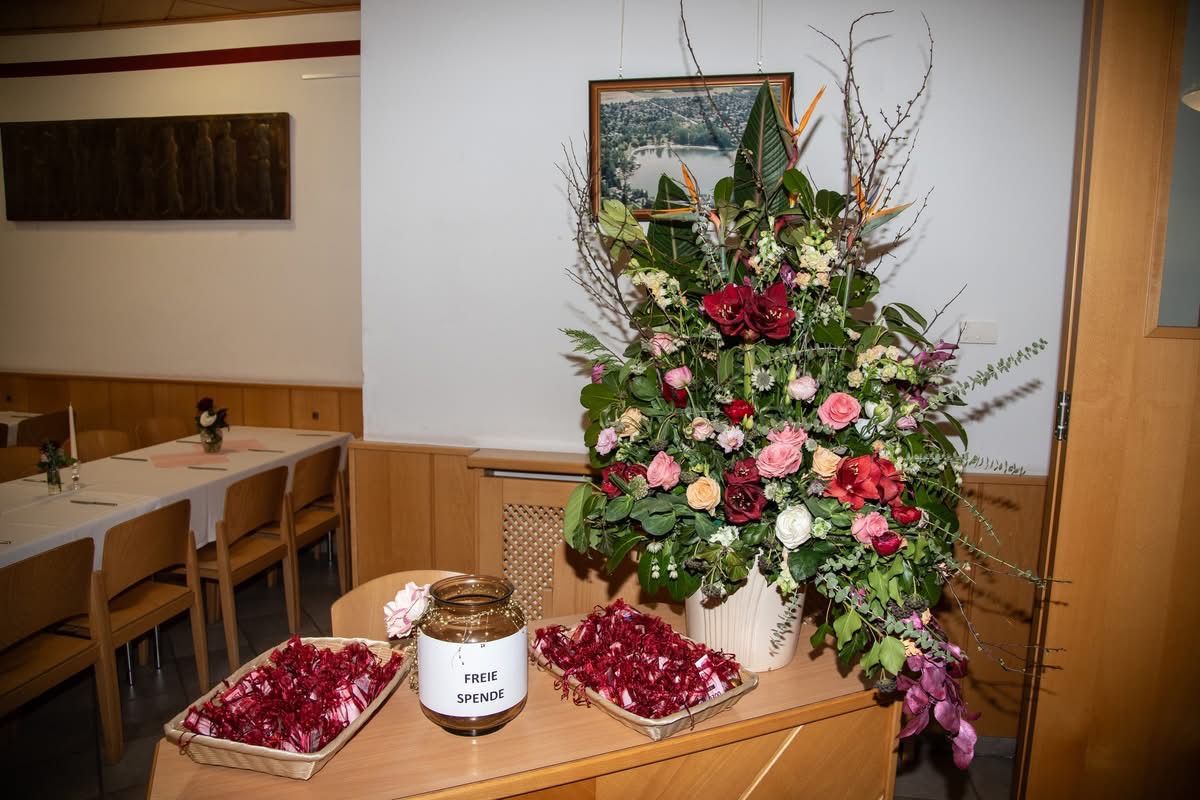 Ein Holztisch mit zwei Körben voller roter Süßigkeiten, einem Glas und einer großen Blumenarrangement mit einem Bilderrahmen dahinter.