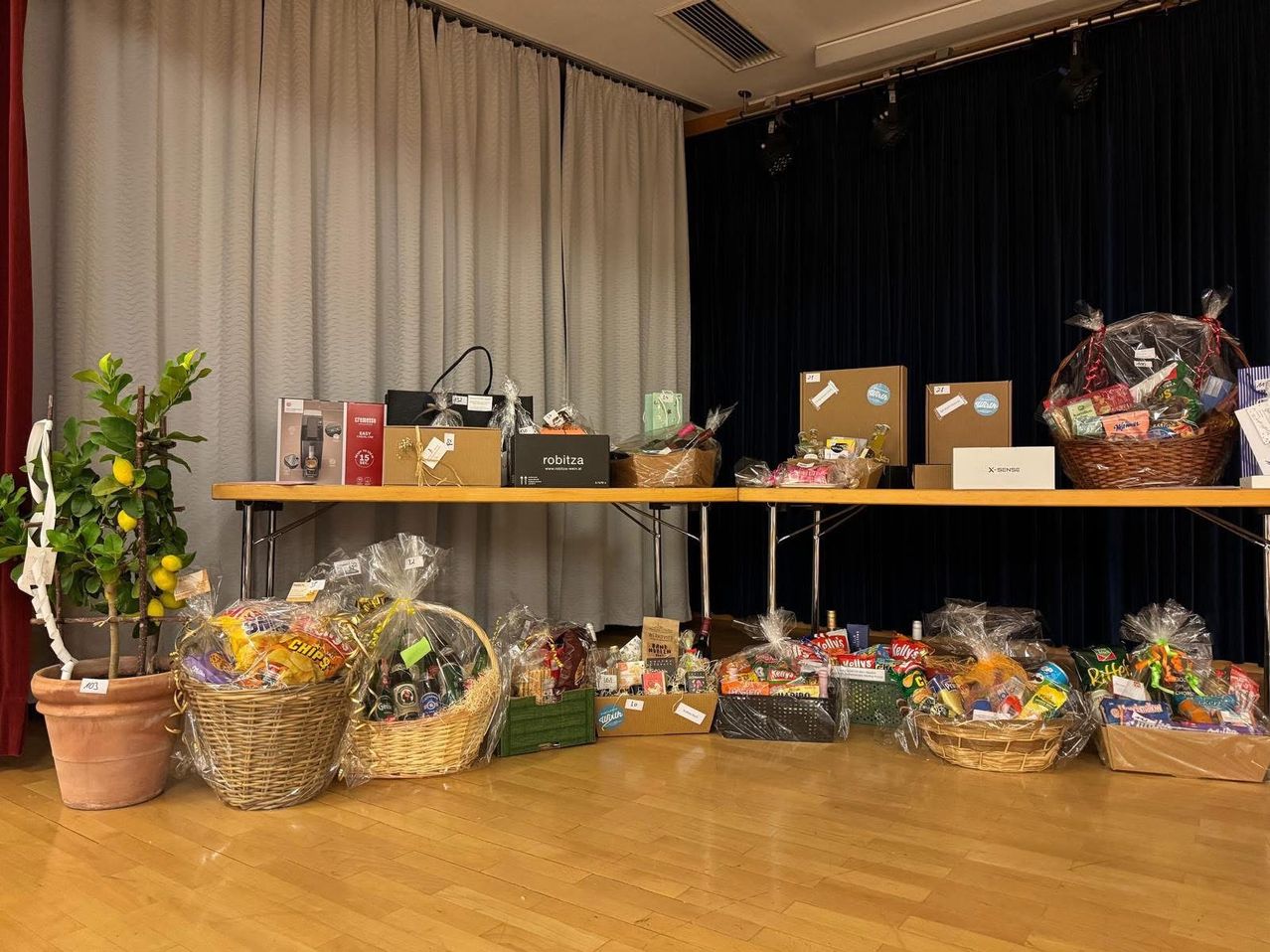 Ein Raum mit Holzboden und Tischen, die mit verschiedenen Geschenkkörben und Kisten bedeckt sind. Vorhänge hängen an den Wänden hinter den Tischen.