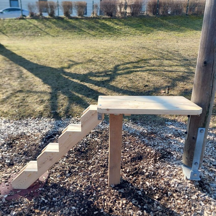 A wooden staircase is installed on the ground, possibly for pets, in a grassy area with a shadow on the ground.