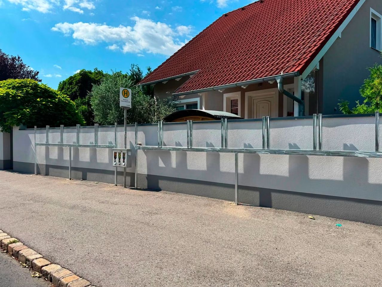 Ein Haus mit einem roten Dach und einer weißen Wand mit einem Metallzaun davor.
