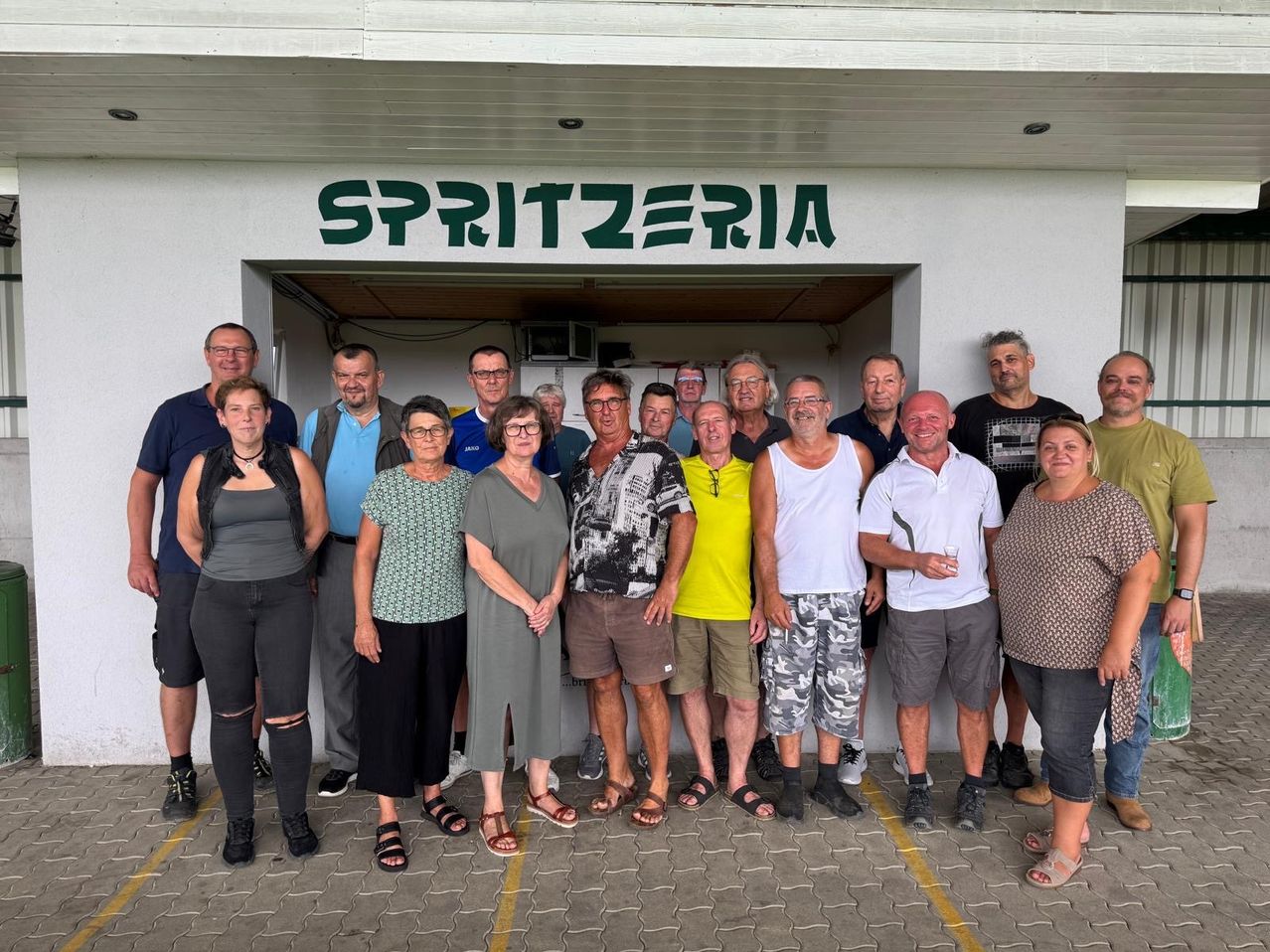 A group of people posing for a photo in front of a building with the word Spritzeria on it.