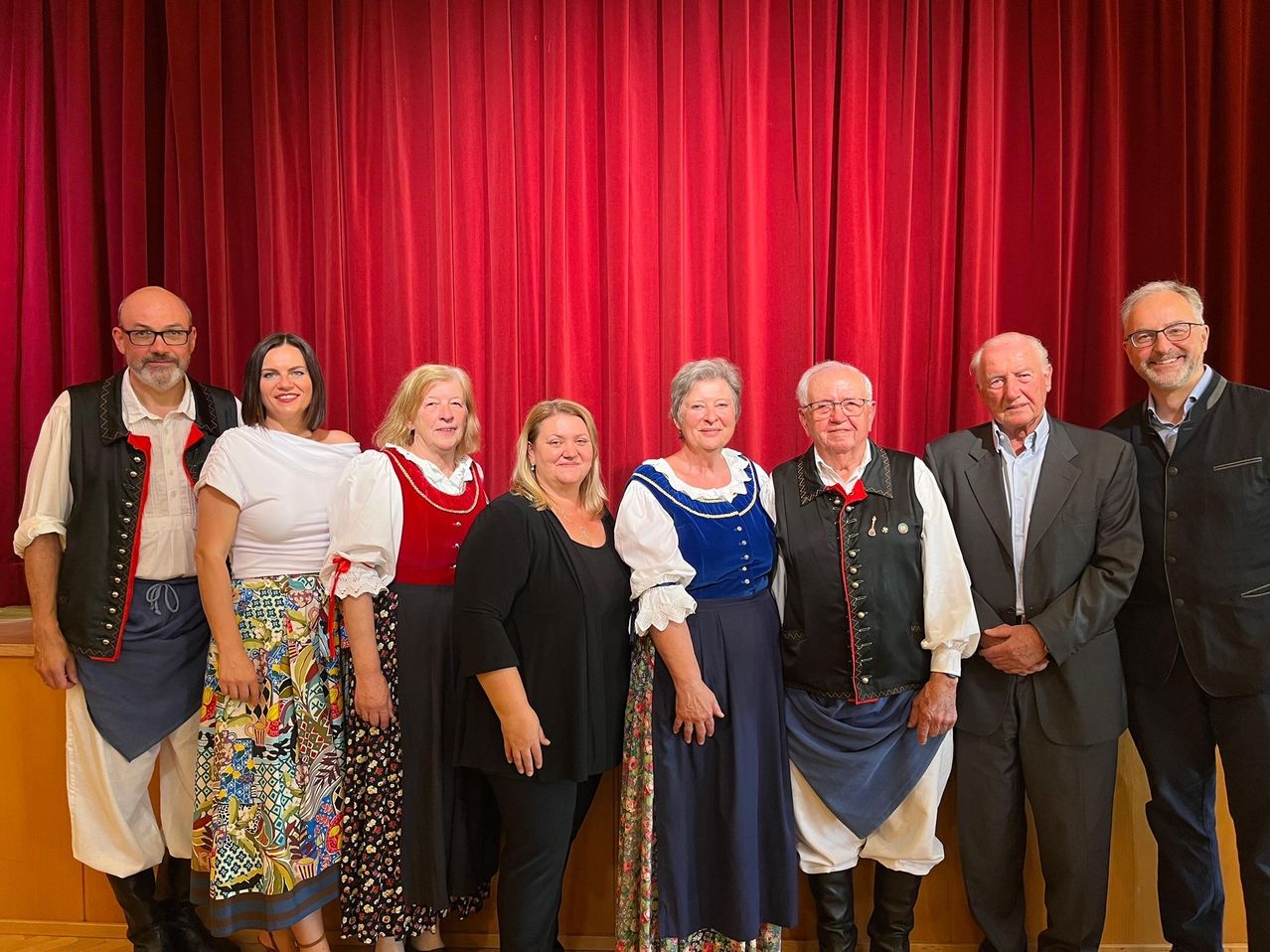 Eine Gruppe von Menschen in traditioneller Kleidung posiert vor einem roten Vorhang für ein Foto.